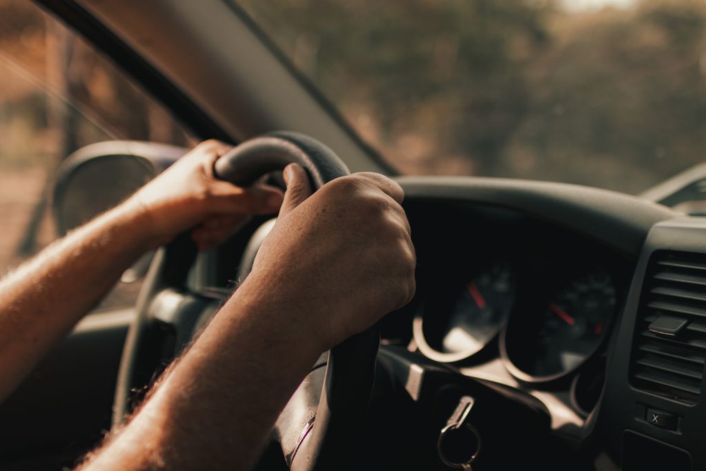 Driver's hands on a steering wheel inside a vehicle, focusing on the act of driving.